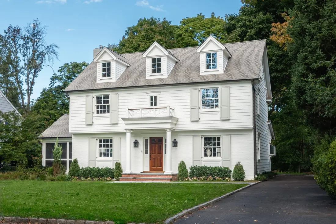 White clapboard home with dormers, a covered front porch and black shutters in Summit, New Jersey